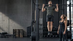 Mann utfører en pull-up med treningspartner ved siden av i et treningssenter.