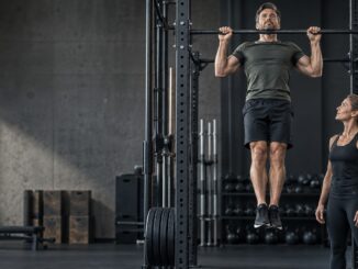 Mann utfører en pull-up med treningspartner ved siden av i et treningssenter.