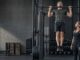 Mann utfører en pull-up med treningspartner ved siden av i et treningssenter.